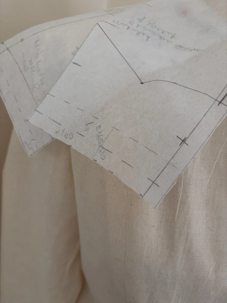 A marked paper pattern pinned to pale cloth.