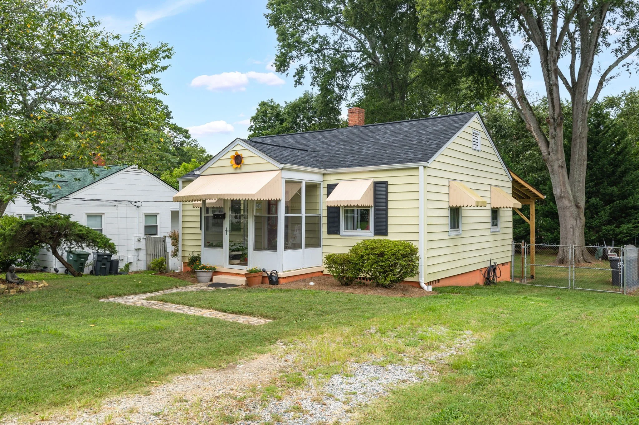 My Sister's House, a yellow 1949 cottage with terracotta and peach awnings, a screened porch, and a shaded lawn at 1007 Grayland St, Greensboro NC, a pet friendly whole home Airbnb near UNCG and Cone Health