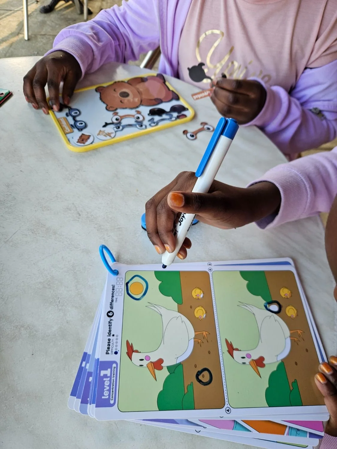 A child marking a spot-the-difference card at a cafe table