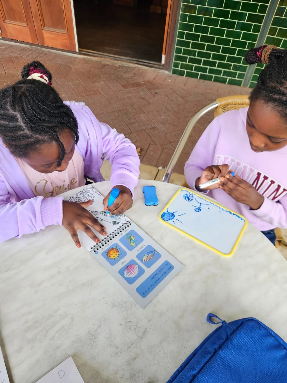 Two children using the water colouring book and the whiteboard at a cafe table