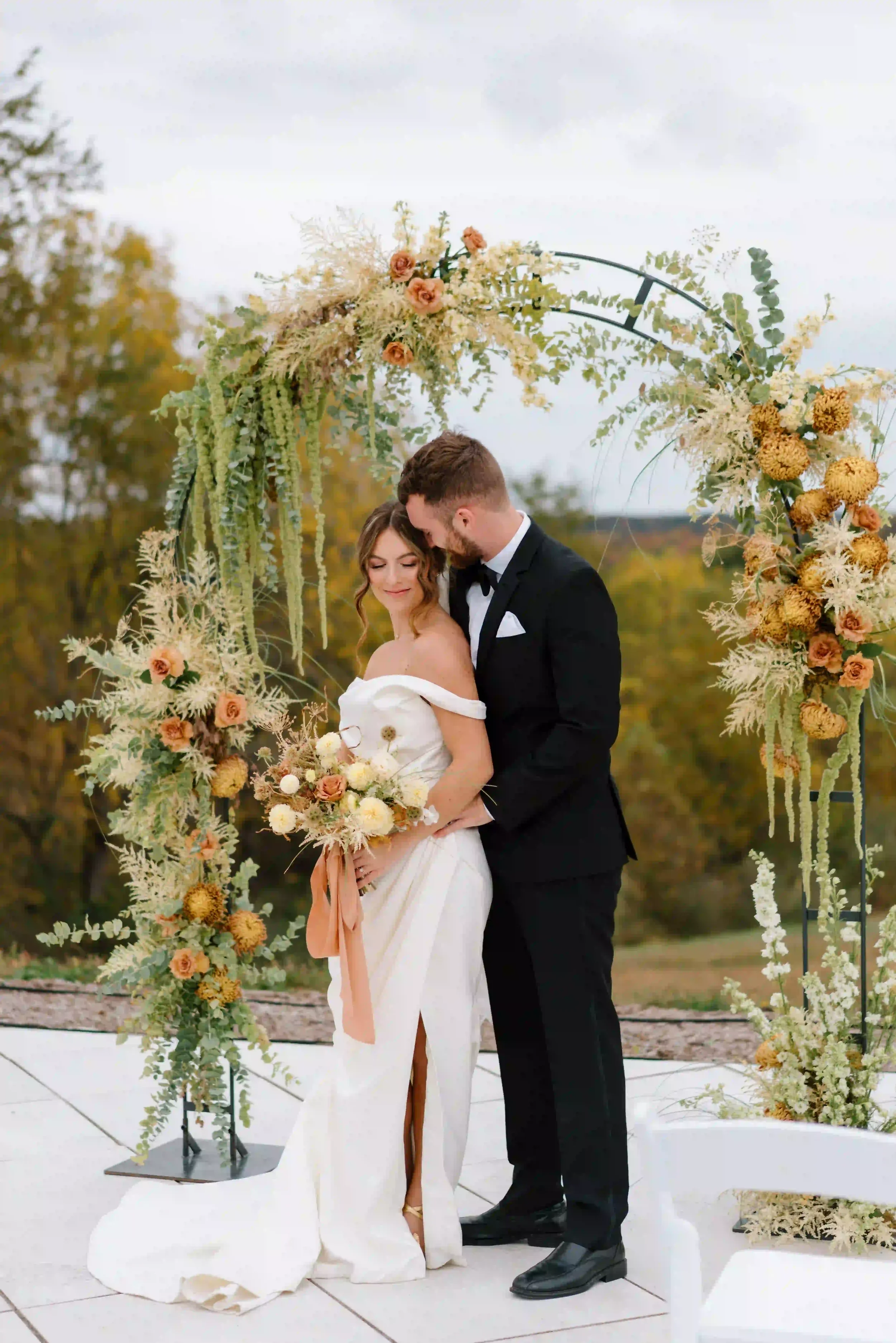 Outdoor wedding ceremony beneath a floral arbor overlooking the hills