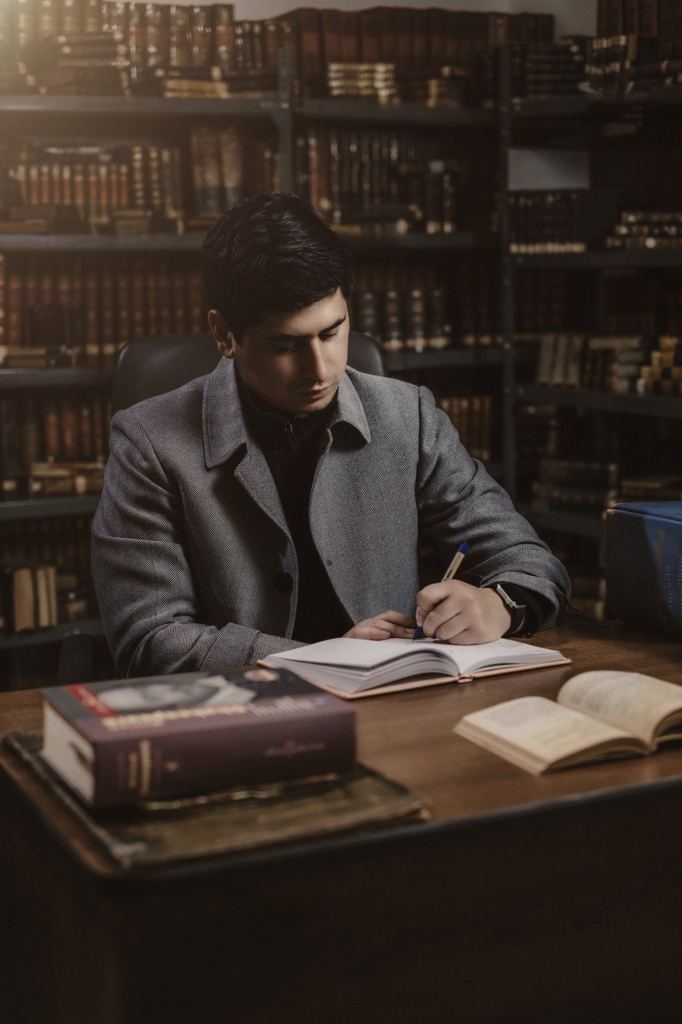 Hombre escribiendo en un cuaderno ante una mesa con libros.