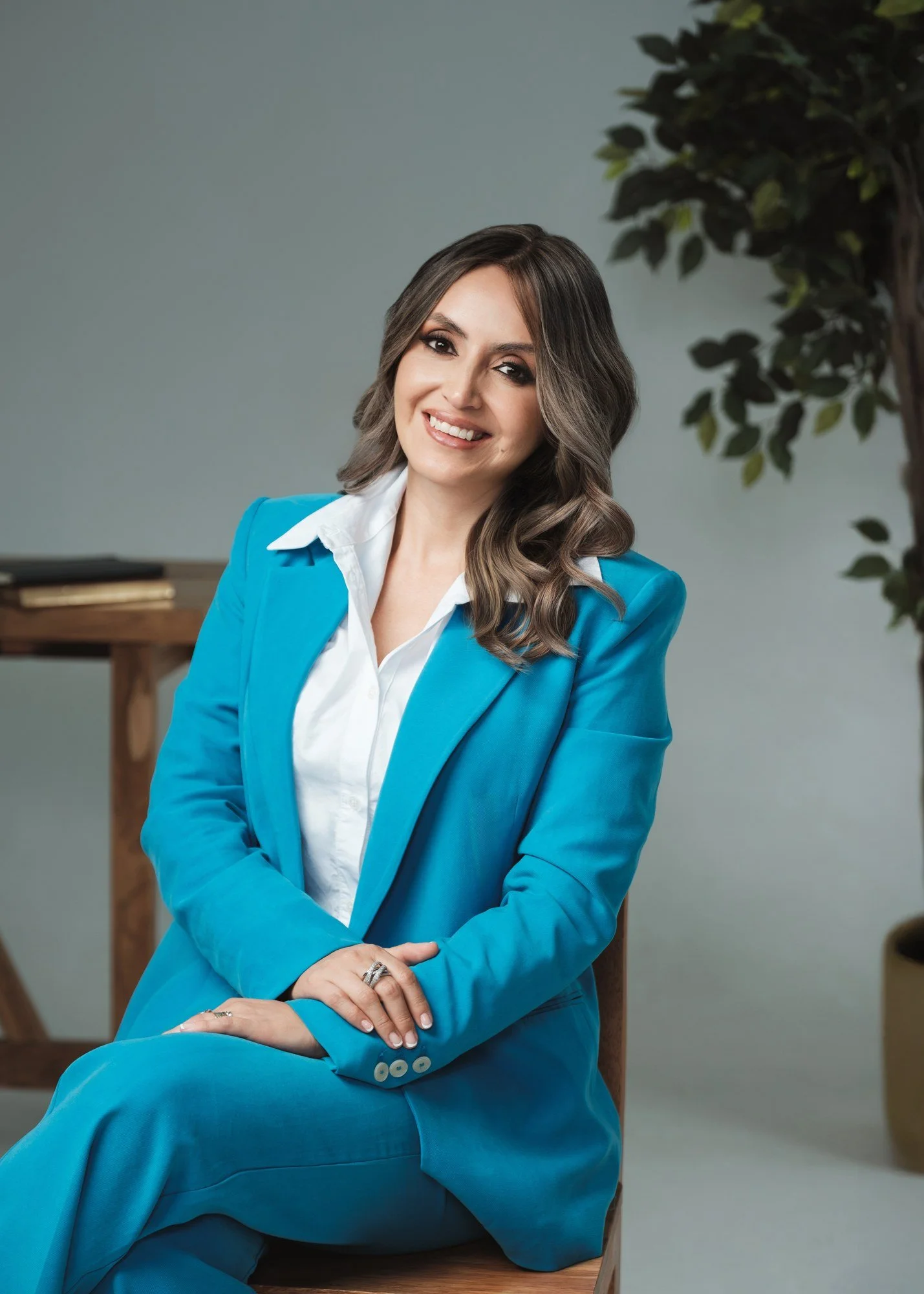 Mujer con traje turquesa sentada y sonriendo a cámara.