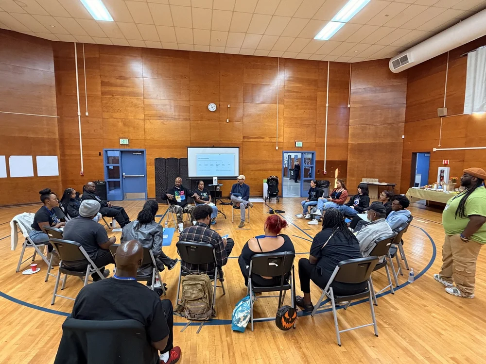 Nicodemus facilitating a circle of community members seated in a school gym