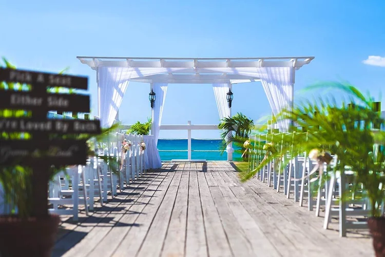 Oceanfront wedding ceremony venue in Jamaica with a wooden aisle, white chairs and a draped arbour