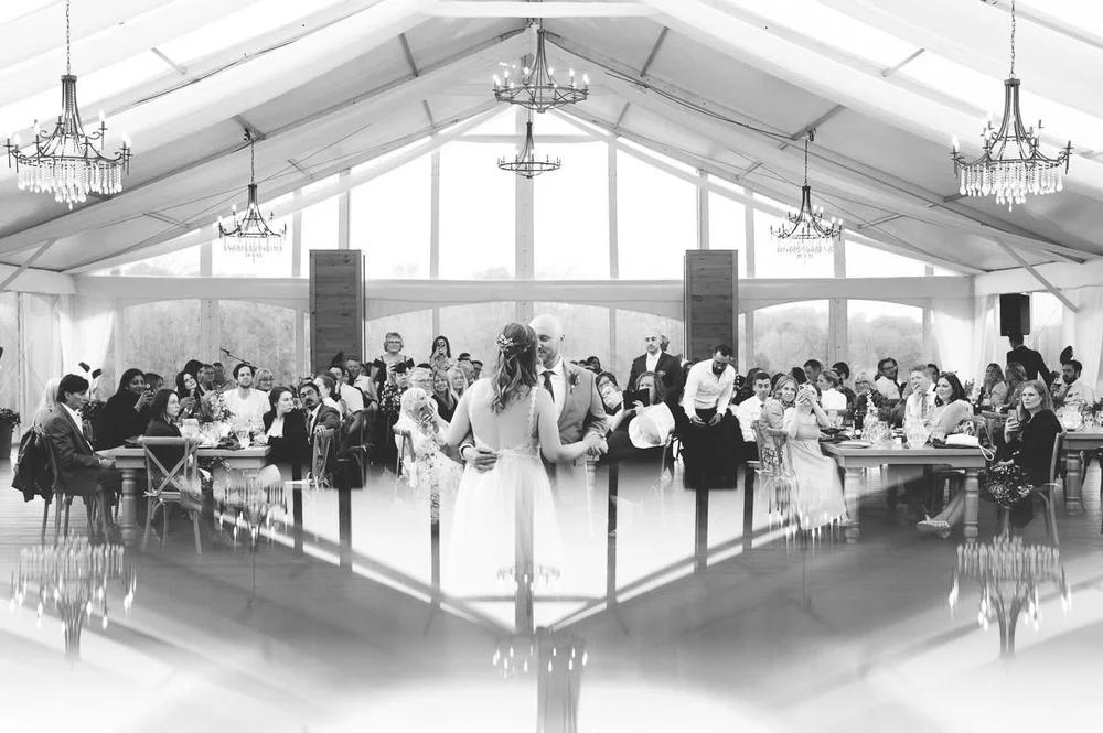 Black-and-white photograph of a couple dancing beneath chandeliers in the reception tent at Glen Oro Farm