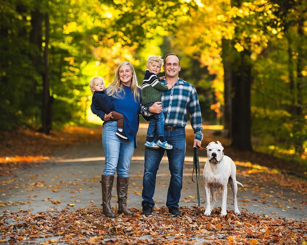 Family of four with their dog on a tree-lined path in autumn