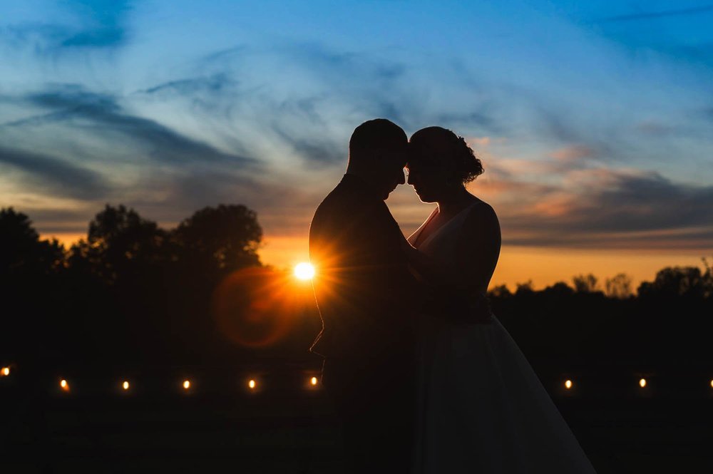 Silhouette of newlyweds kissing as the sun sets behind them