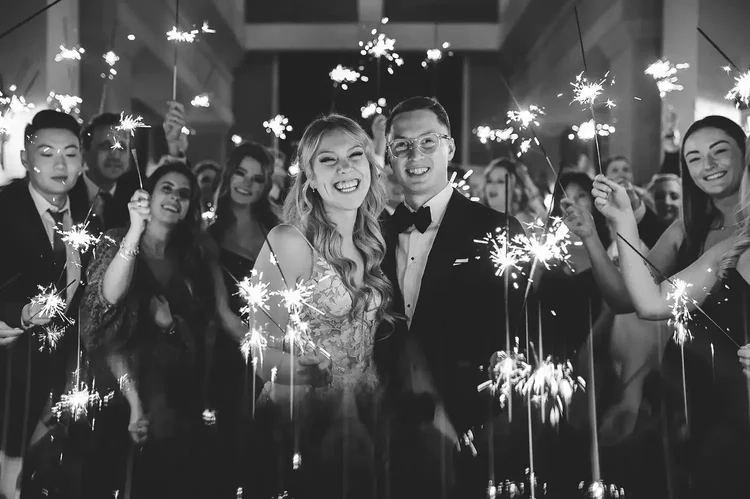 Newlyweds laughing with guests holding sparklers at their wedding reception