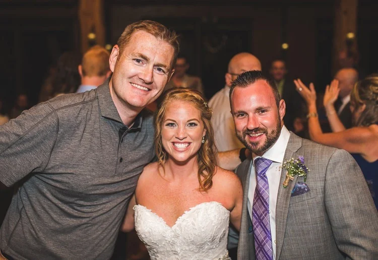 Vaughn Barry smiling with a bride and groom at their wedding reception