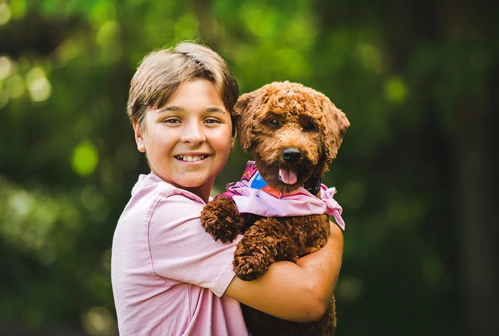 Child smiling while holding a curly-haired dog