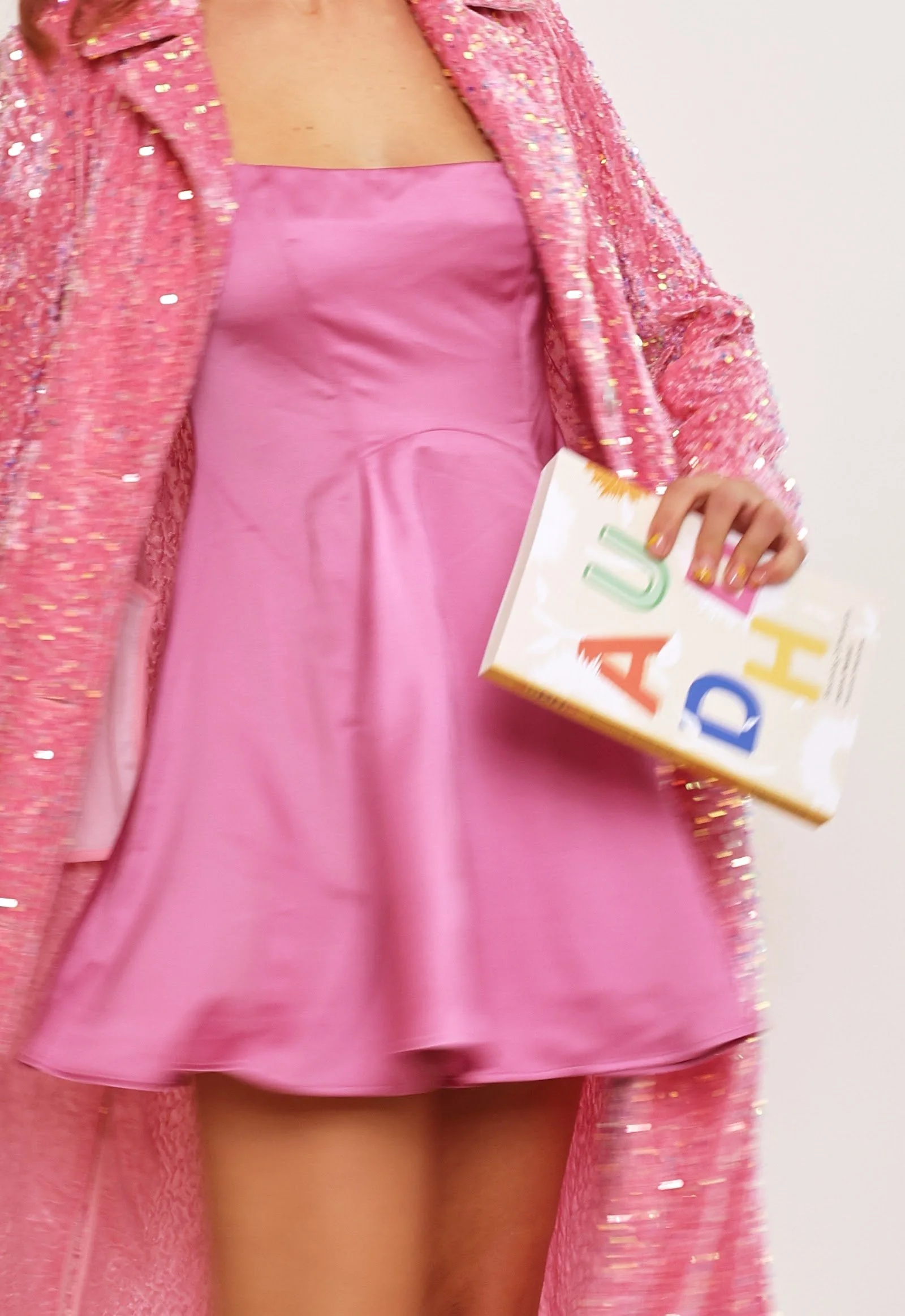 Pink sequinned jacket and pink dress, holding the book AuDHD: Blooming Differently