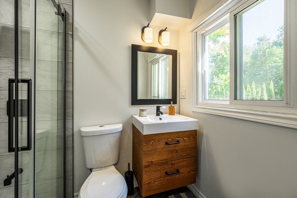 Renovated bathroom with wood vanity, black fixtures and glass shower