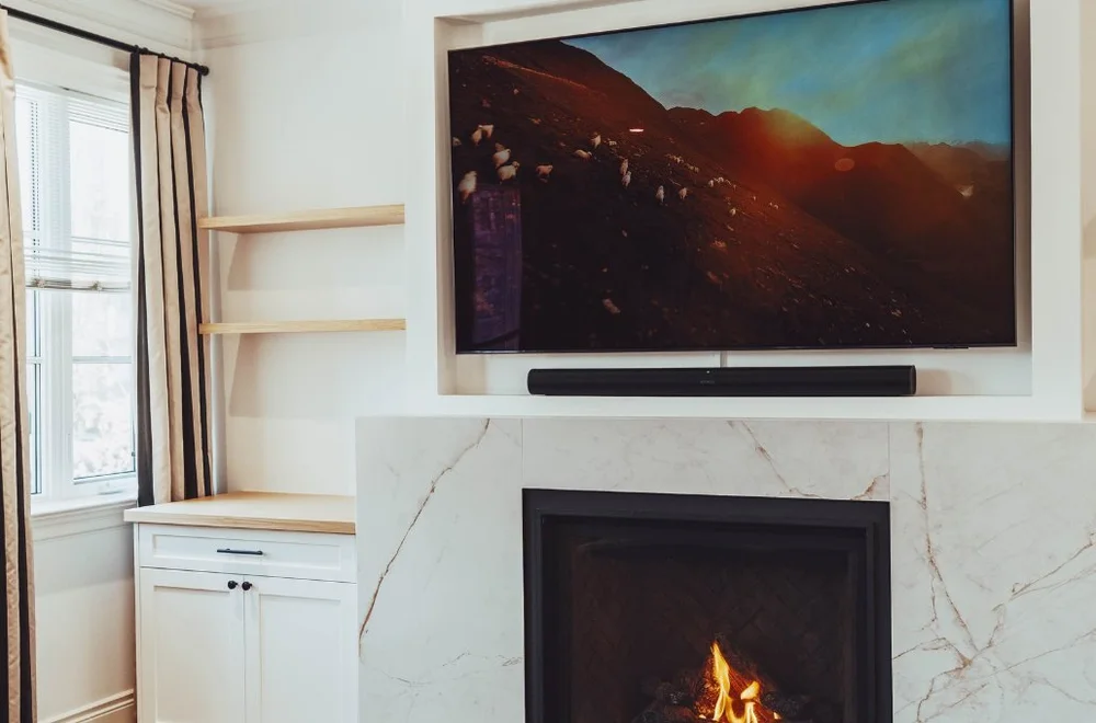 Wall-mounted TV above the marble fireplace with built-ins