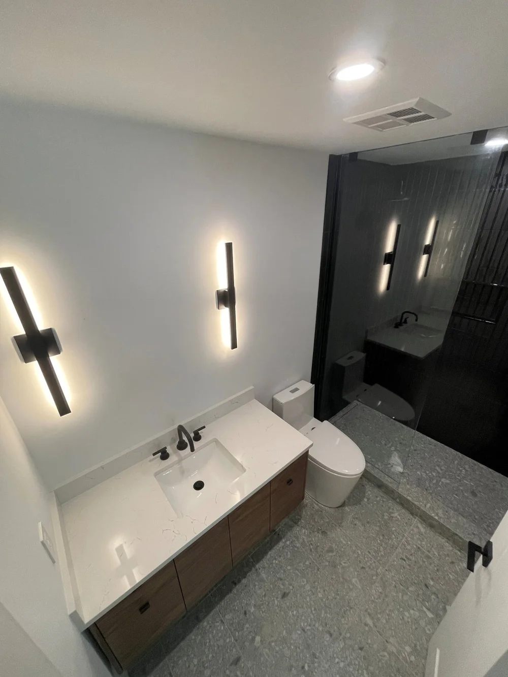 Terrazzo-look floor tile and black-tile shower in the renovated condo bathroom