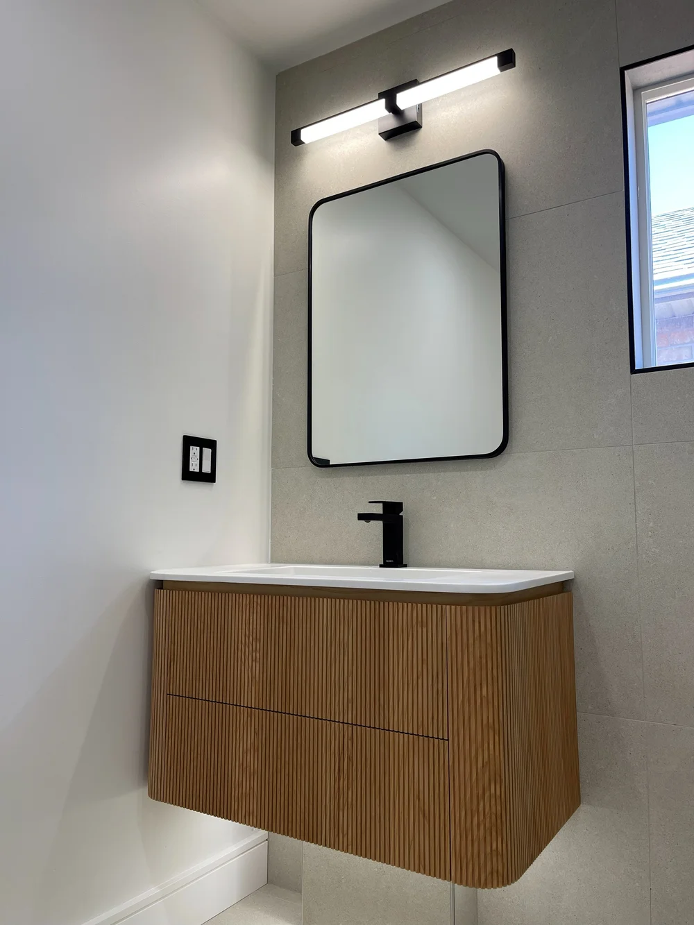 Curved wood floating vanity with matte black faucet and mirror in Vaughan