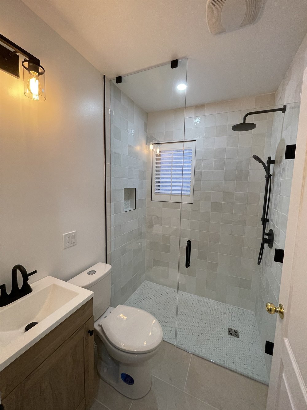 Glass shower with handmade-look square tile, pebble floor and matte black fixtures