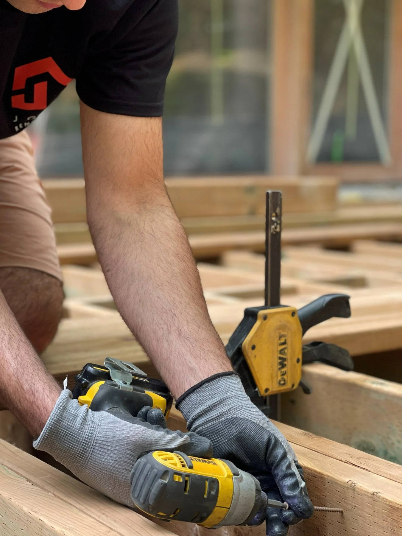 J Group Renovations crew member in a company shirt and work gloves fastening new deck framing with an impact driver