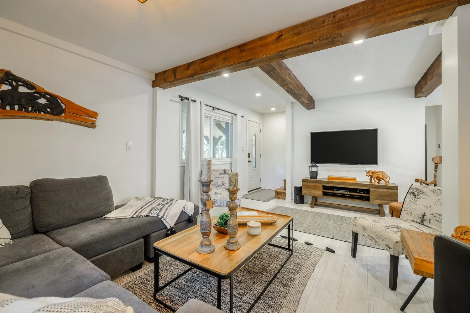 Renovated open-concept living room with exposed wood beams and pot lights