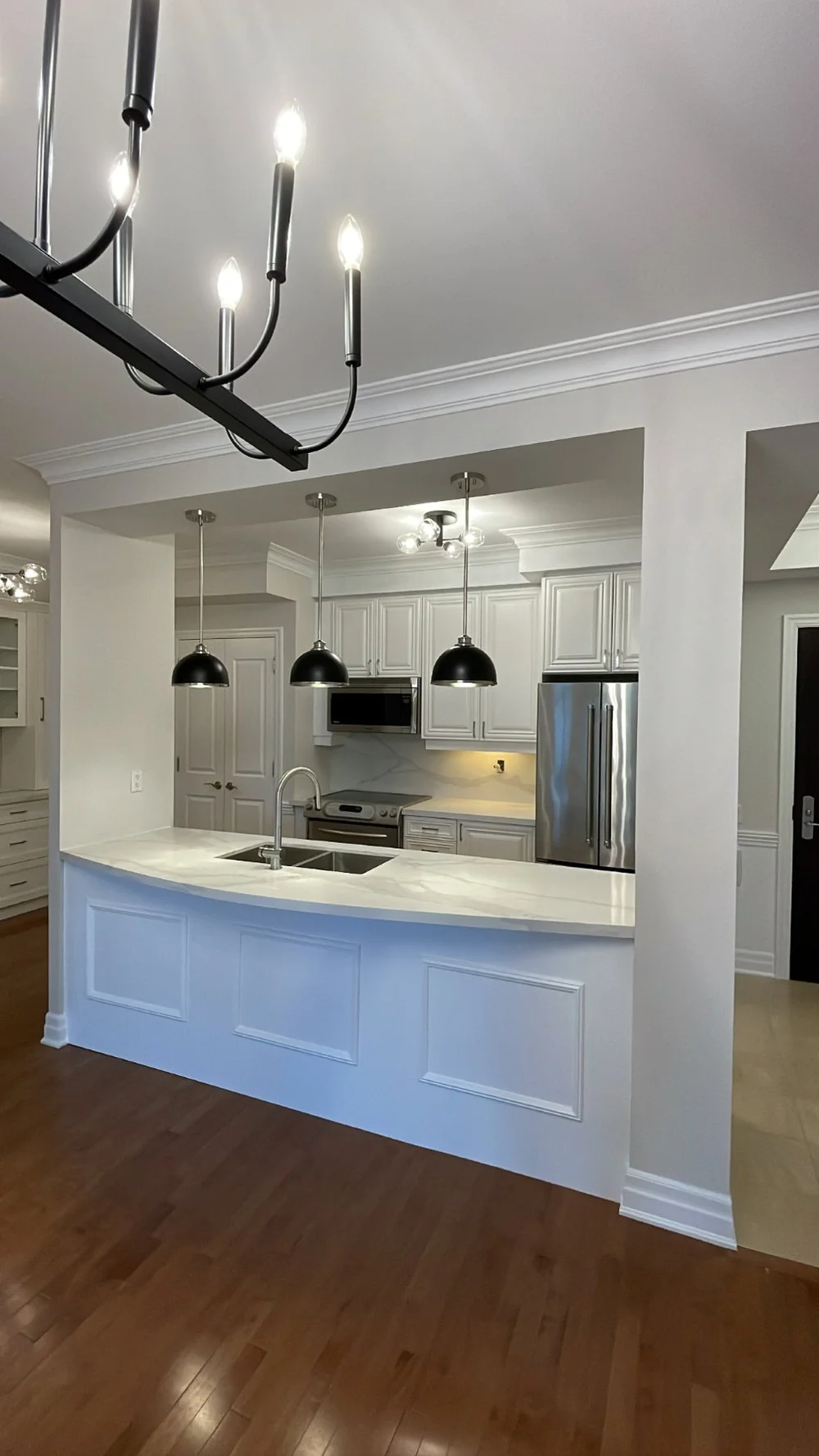 Etobicoke kitchen after the renovation, opened to the living room with a new island, pendants and a black chandelier