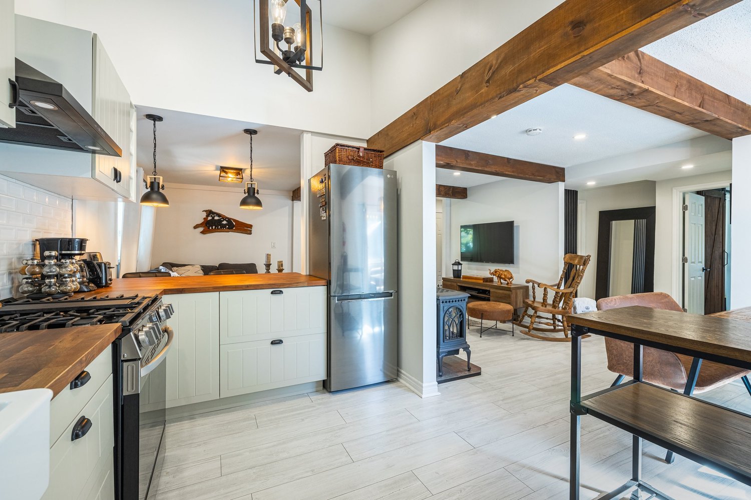 Renovated kitchen with exposed wood beams, white cabinetry and butcher-block counters by J Group Renovations