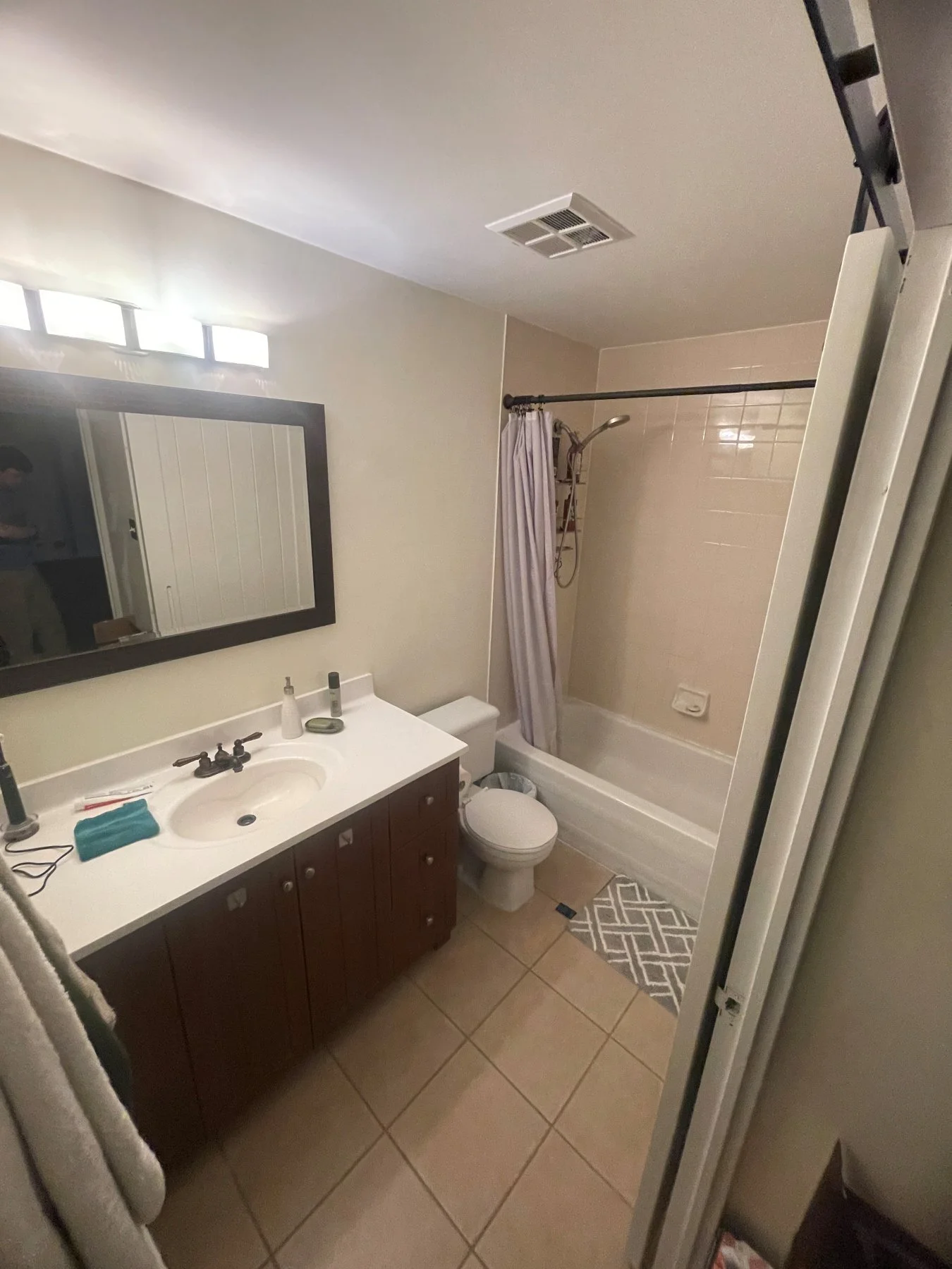 Distillery District condo bathroom before the renovation, with a tub-shower, beige tile and dark vanity