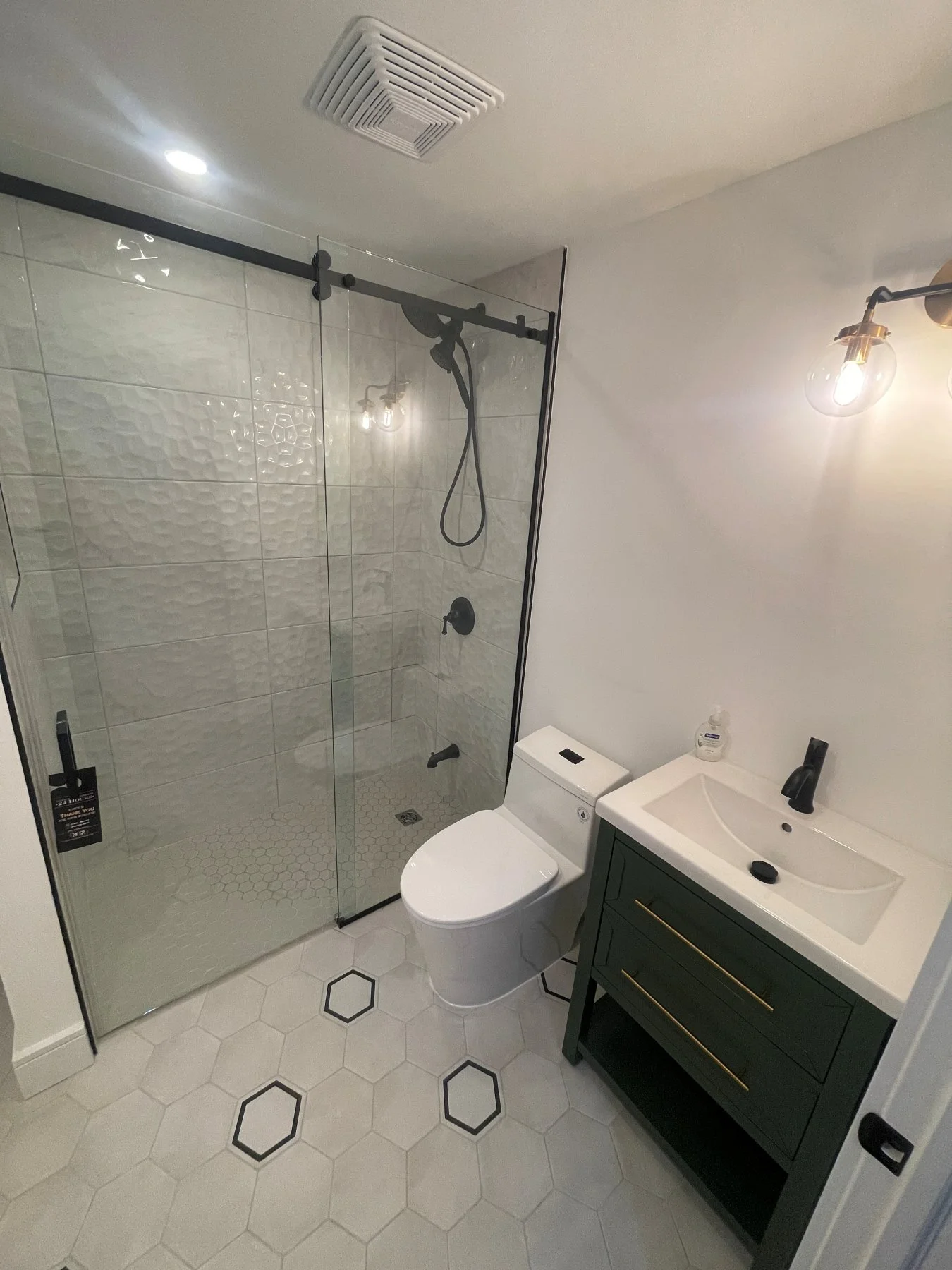 Etobicoke bathroom after the renovation, with a sliding glass shower, hex floor tile and green vanity