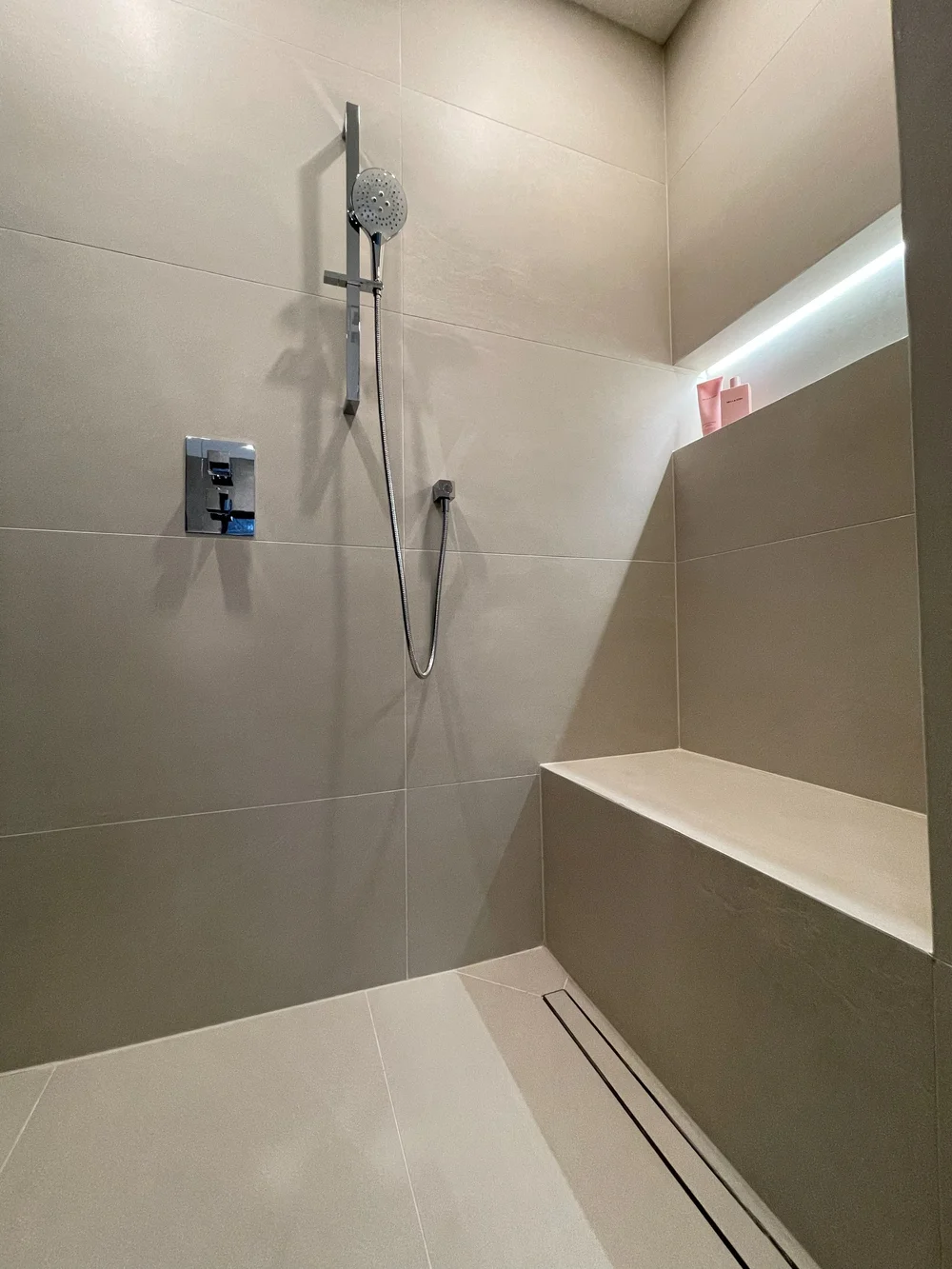 Walk-in shower with a built-in bench, linear drain and lit niche