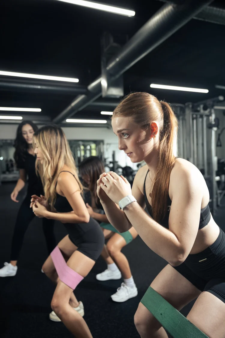 Two women training together in a semi-private banded squat session at Crown Fitness