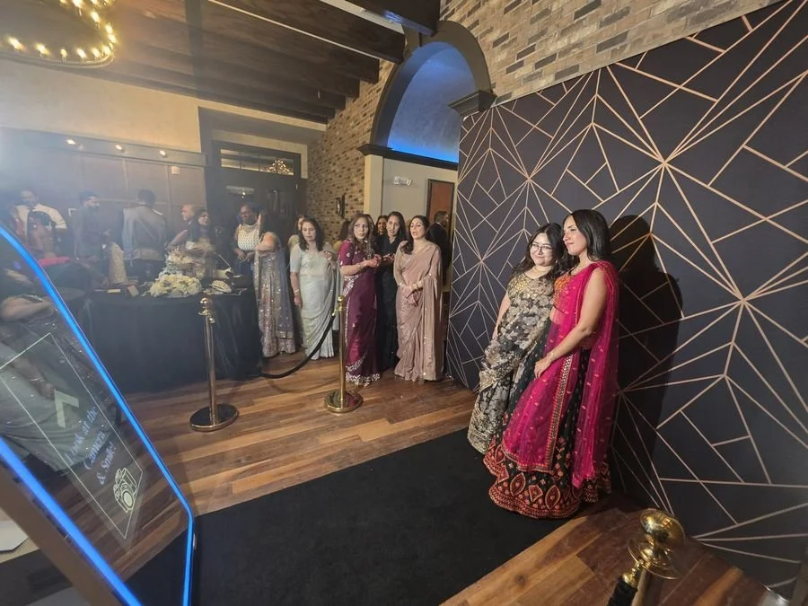 The full photo booth setup: the mirror photo booth, black carpet, gold stanchions and a geometric backdrop at a wedding