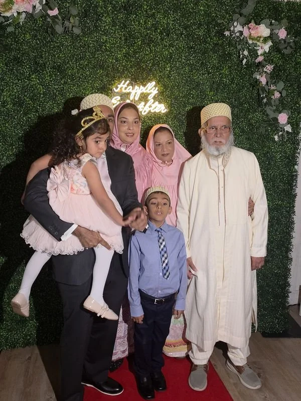 A family on the red carpet in front of the greenery wall with a neon sign