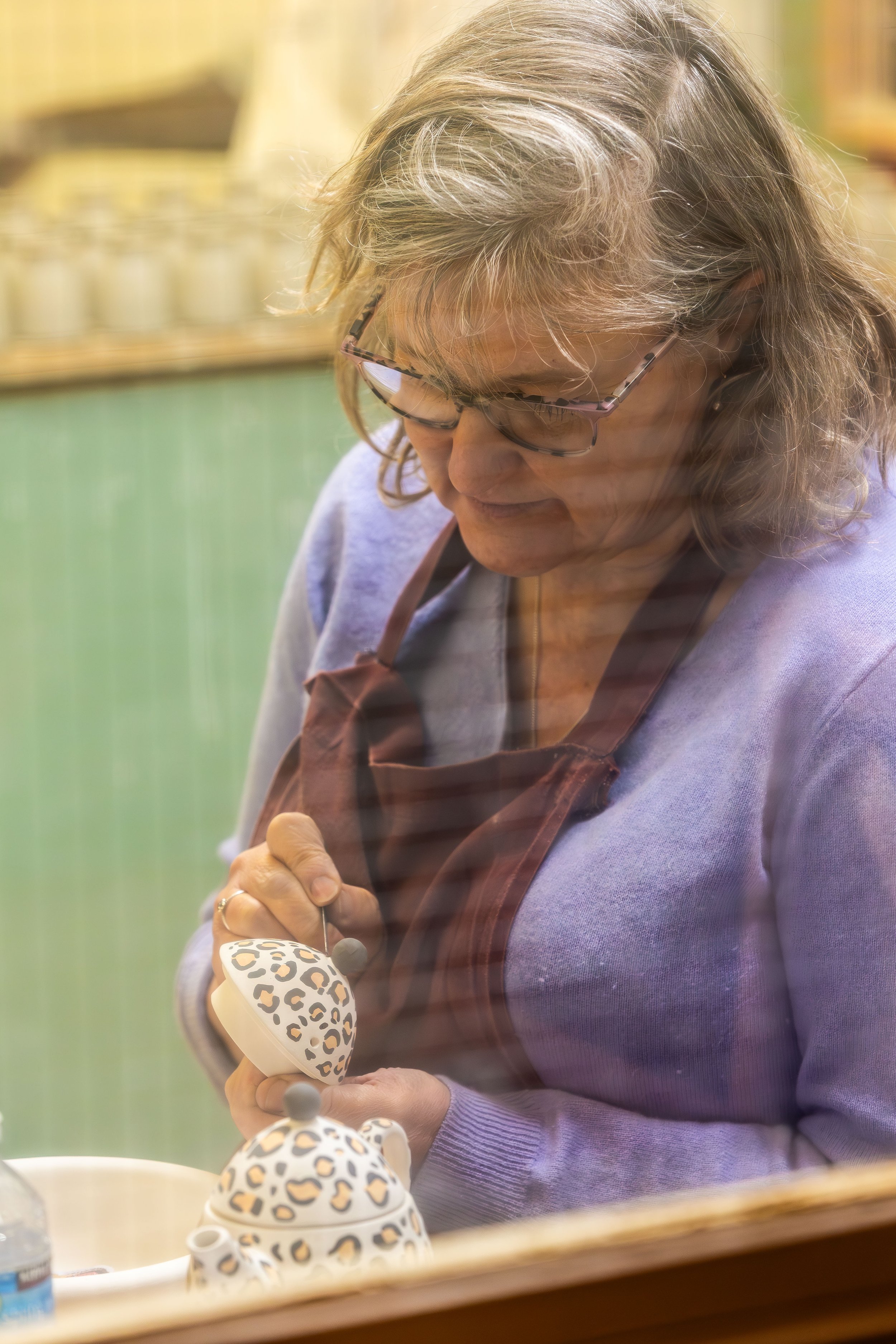 Pottery artist delicately hand-painting teapot lid at The Kiln Café Grayshott Pottery