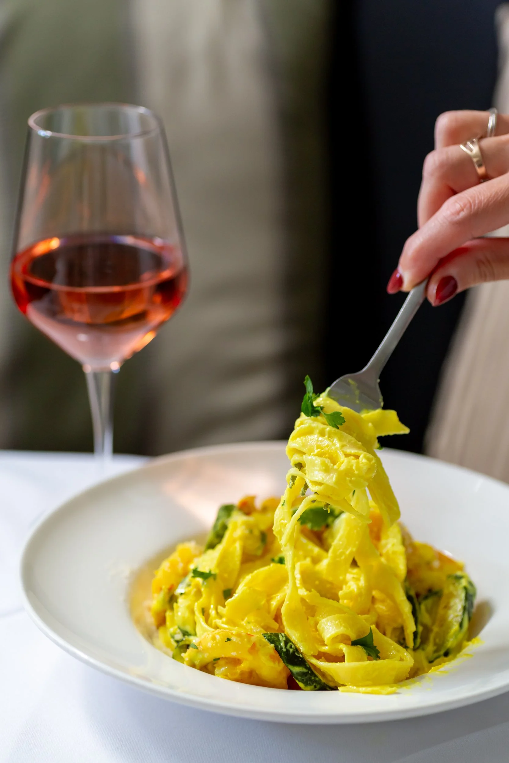 Tagliatelle with courgette and prawns twisted on a fork with glass of rose wine at Carlo Independent Italian Restaurant in Petersfield Hampshire