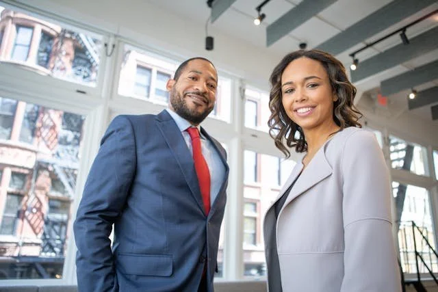 A black man and black woman in business suits, smiling at the viewer