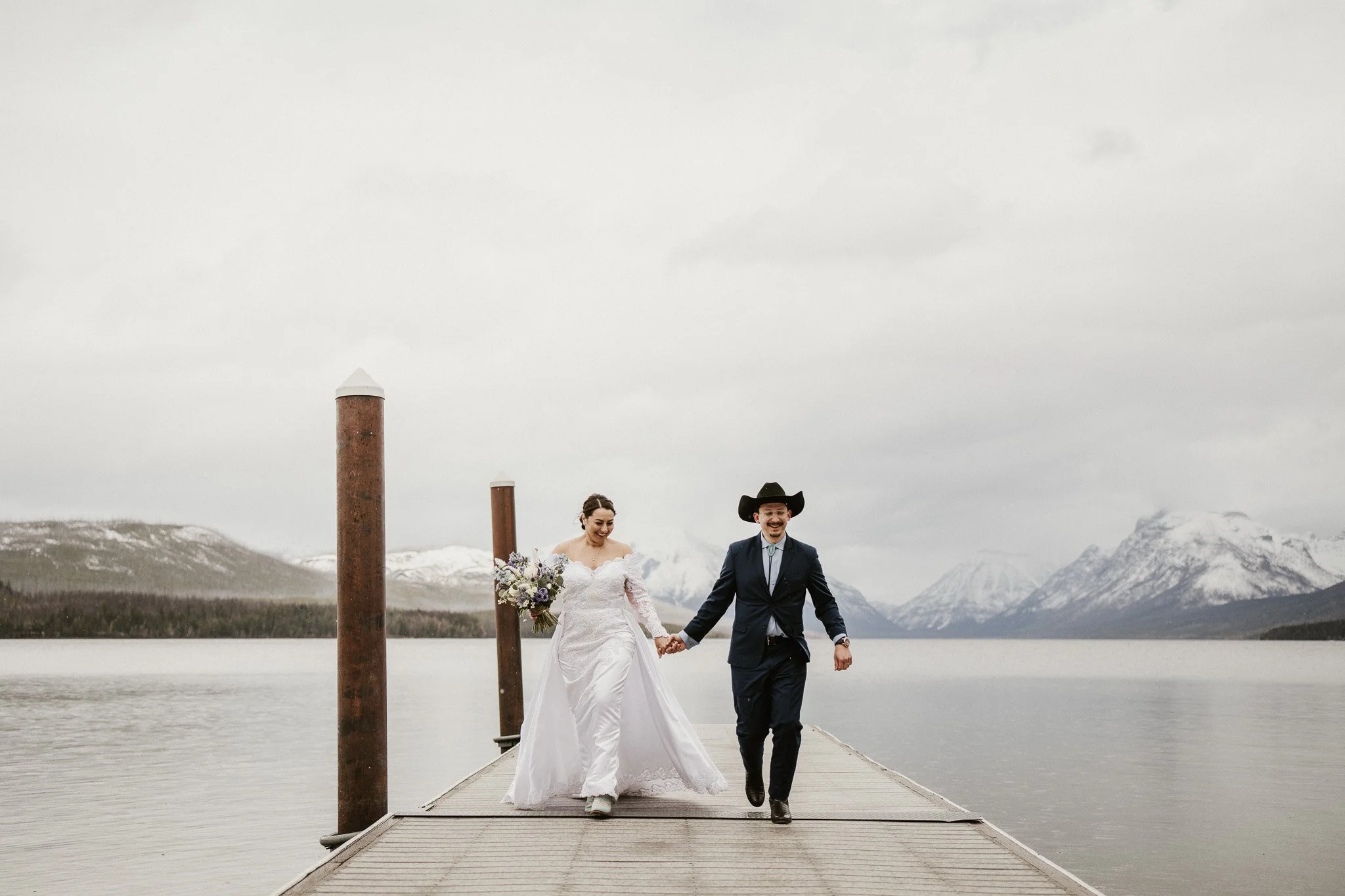 Ian and Rachel standing on the wooden footbridge at Lake McDonald Lodge, creek and rocks below them, trees surrounding