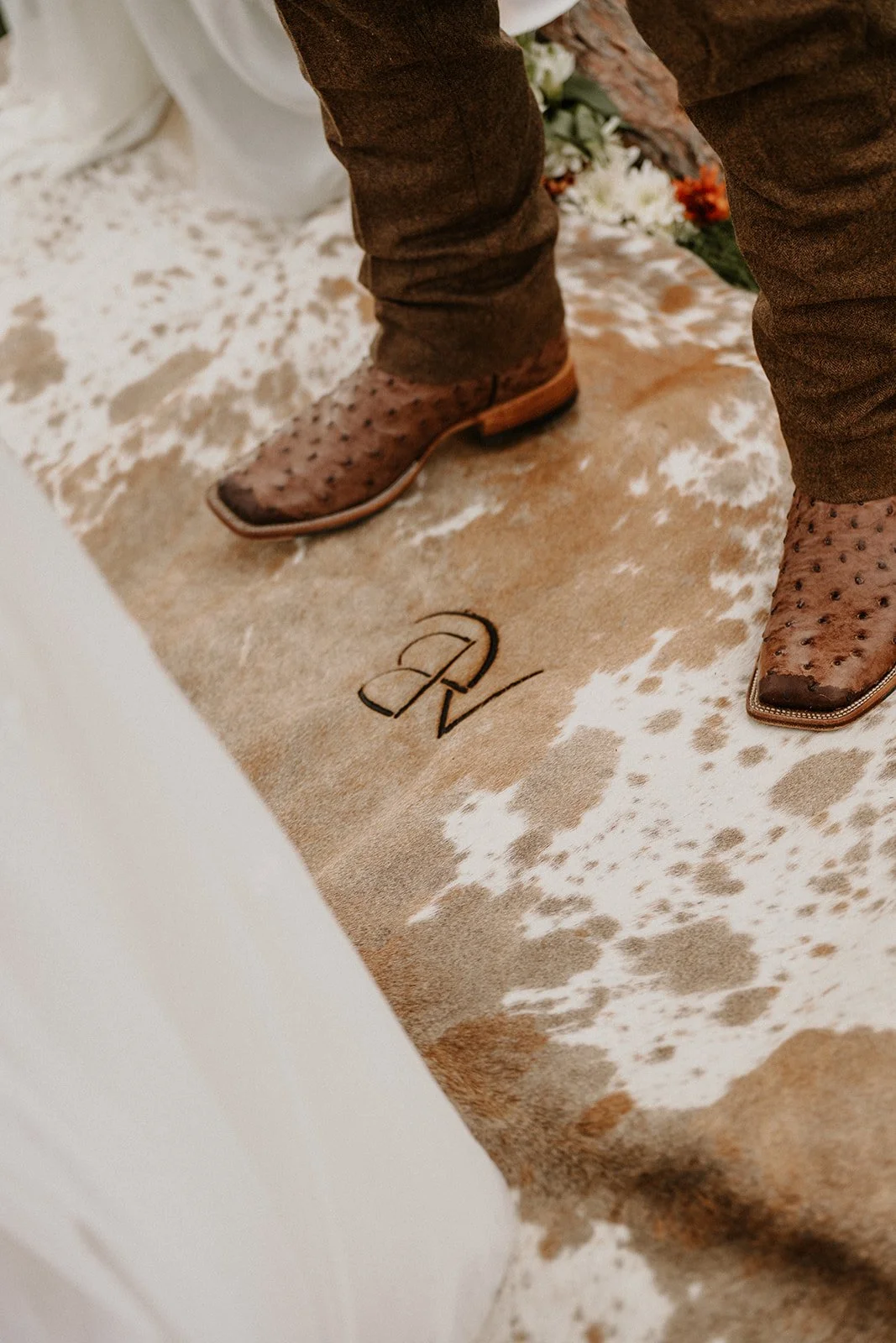 Groom's ostrich cowboy boots on a cowhide aisle runner with monogram at a Western wedding in Kalispell, Montana