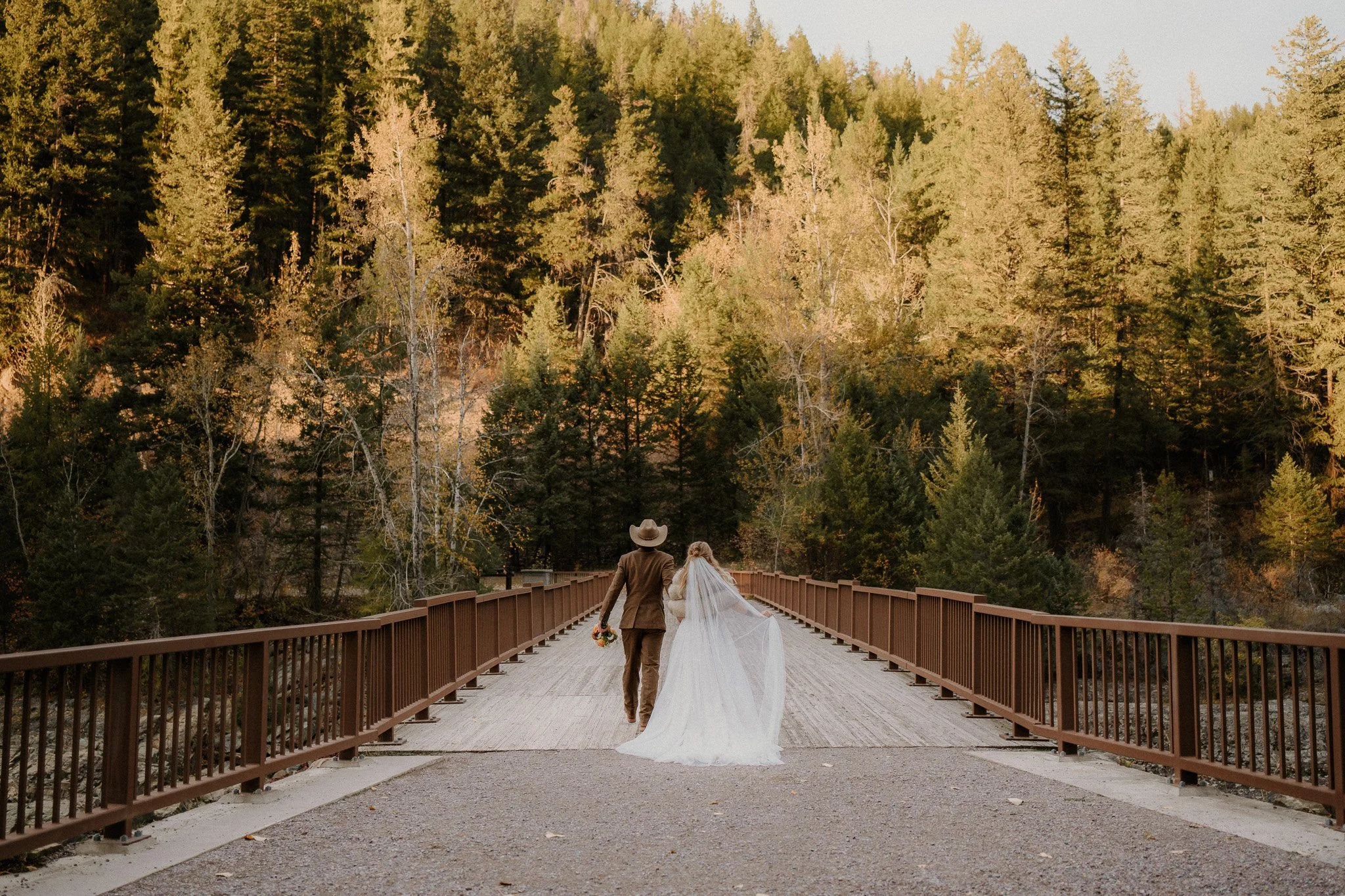 Bride and groom walking through a golden autumn field in Glacier National Park during their day-after session