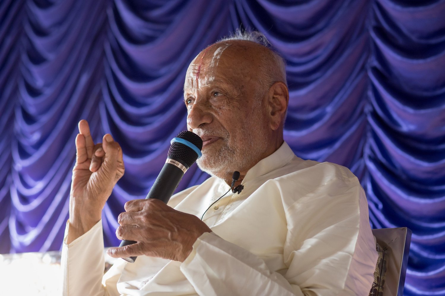 Sri U.Ve. Prof. M.A. Lakshmithathacharya Swami speaking, his right hand raised in Nāsika Mudrā