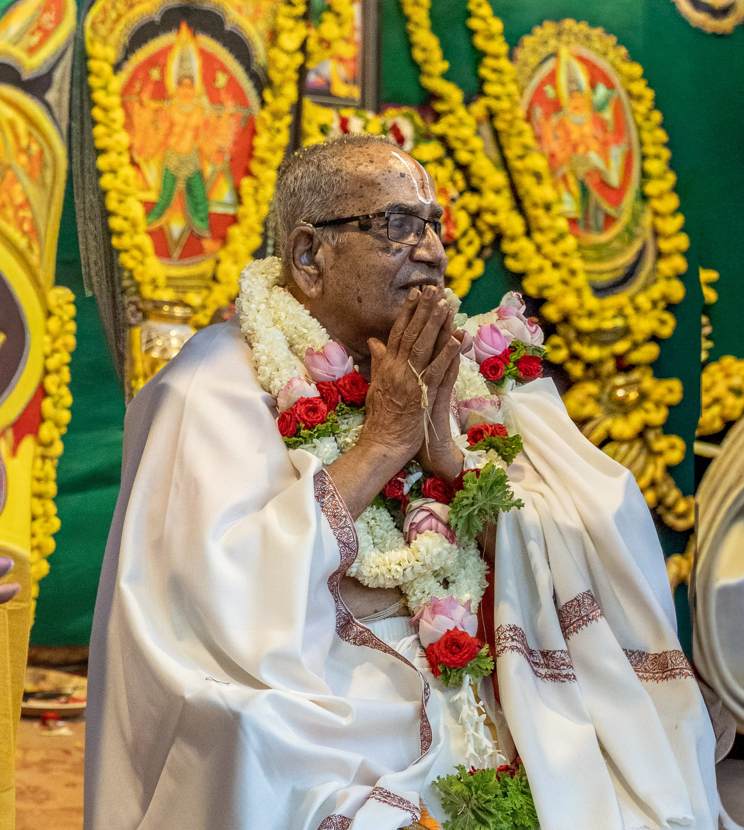 Śrī B.N.S. Iyengar, garlanded with jasmine and roses, his hands joined in greeting