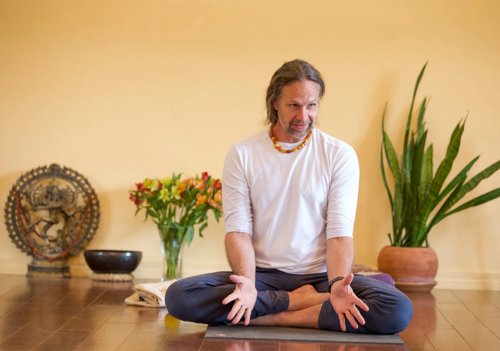 Andrew Eppler seated cross-legged, teaching, against a warm wall