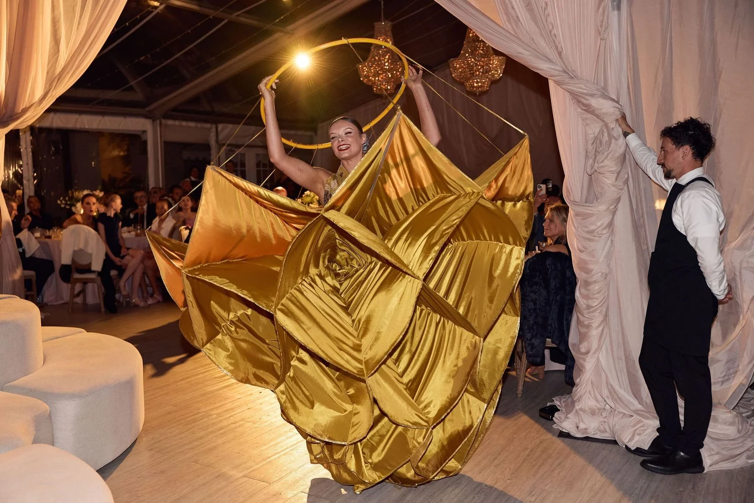 An artist of the House revealing a sweeping gold gown in a marquee