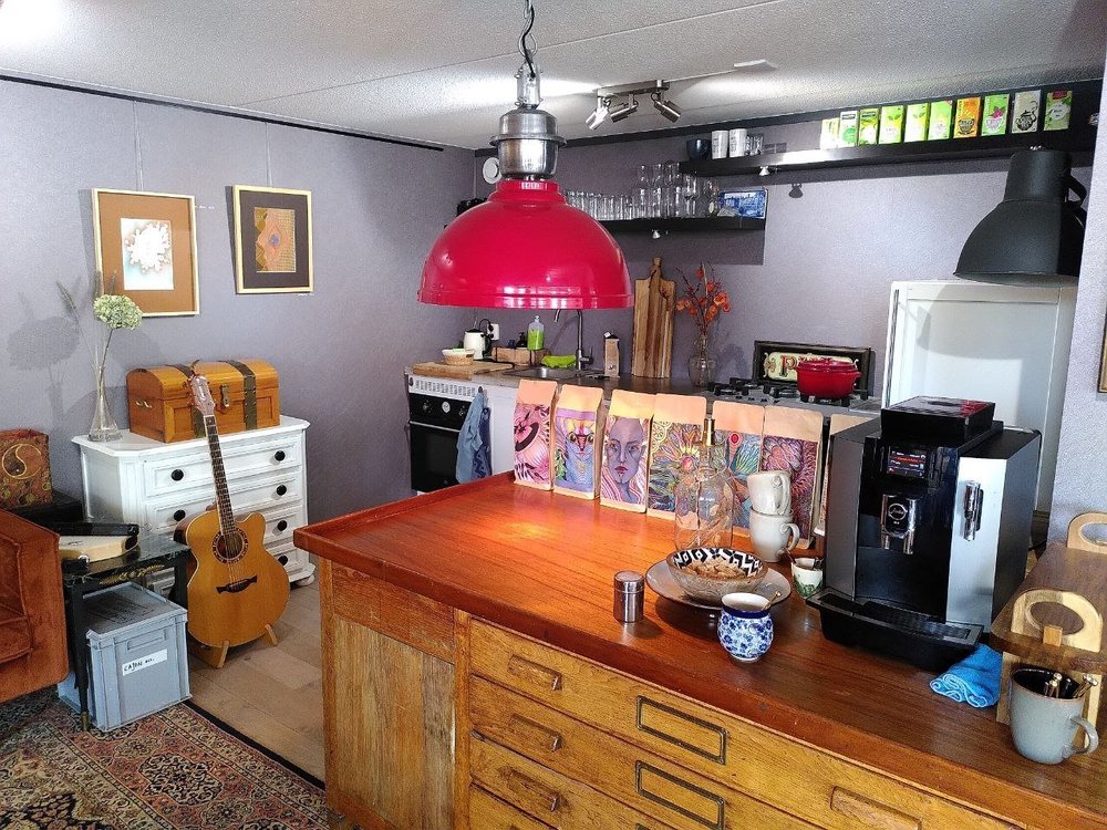 De koffiehoek van Hanzehuis Gallery in Stavoren: een houten bar met rode hanglamp, koffiemachine en kunst van Xandra Dupper aan de muur.