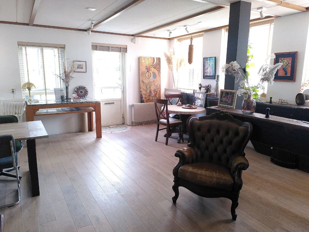 The sitting area of Hanzehuis Gallery in Stavoren: a leather armchair, a round table and art by Xandra Dupper on the walls, with daylight through the windows.