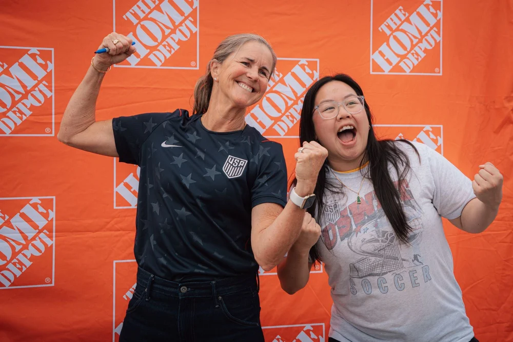 Two fans cheering at a brand backdrop
