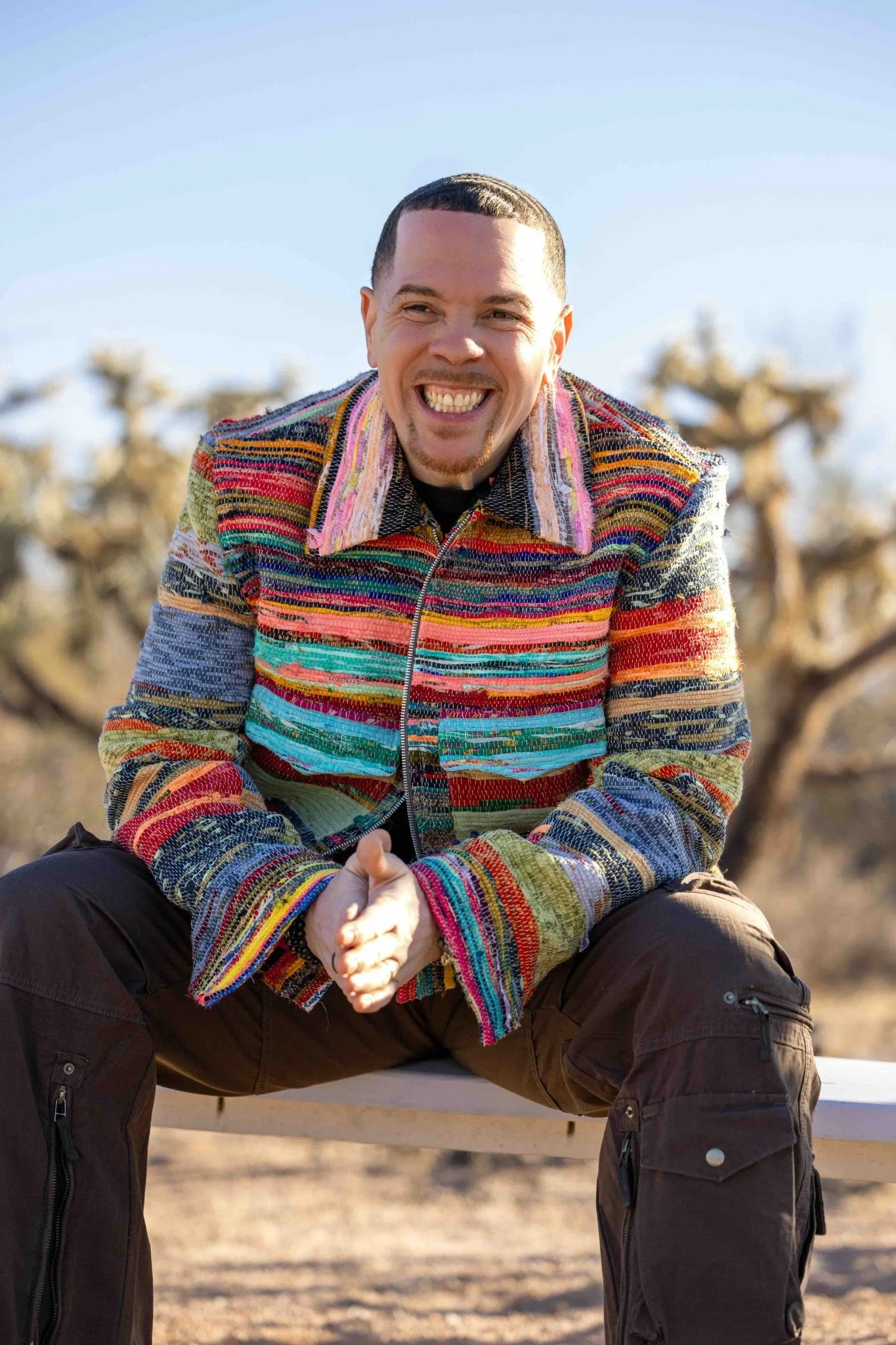 Sean Goode smiling outdoors, seated in a colorful striped jacket.