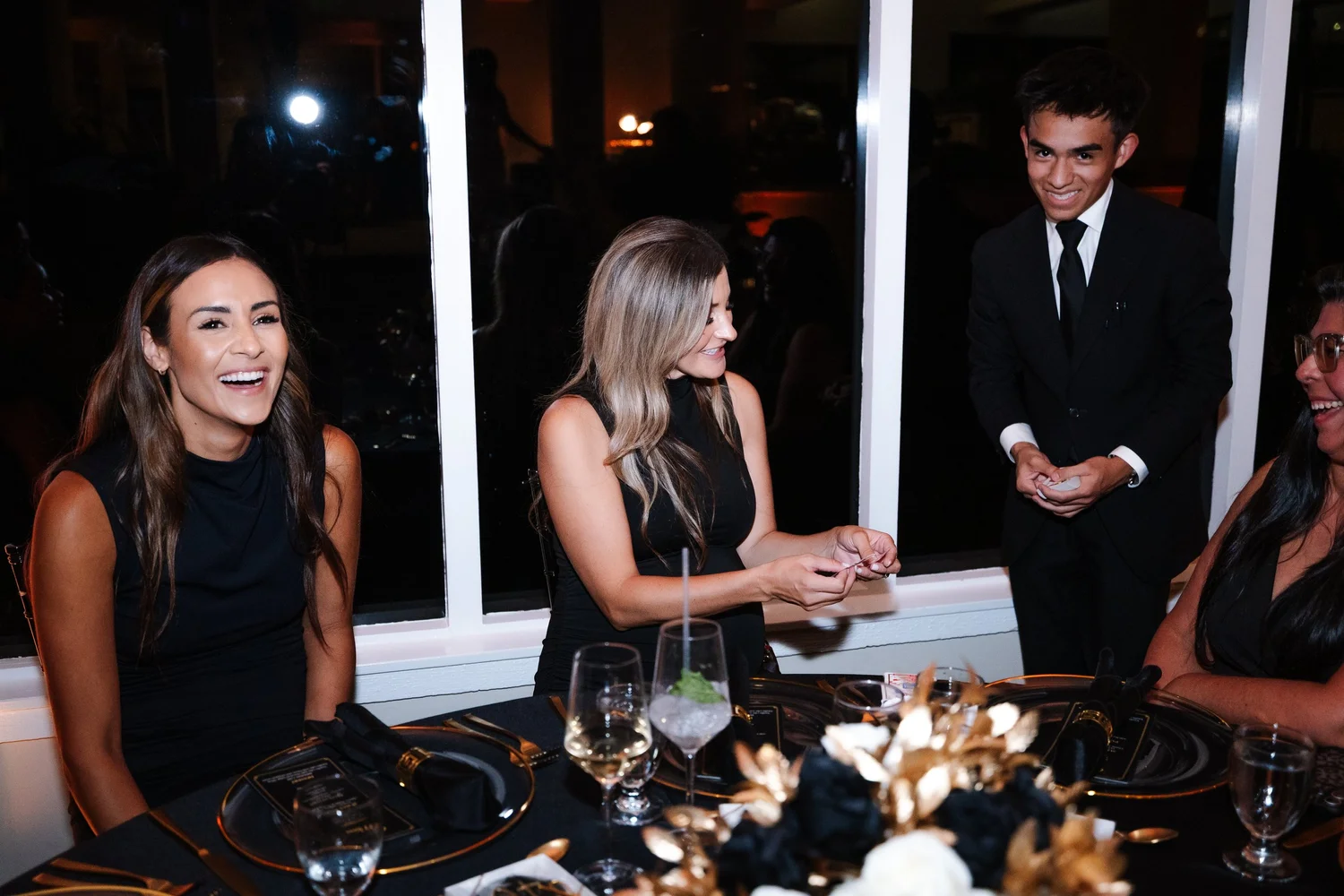 Guests laugh at a dinner table as Jacob Martinez performs strolling magic