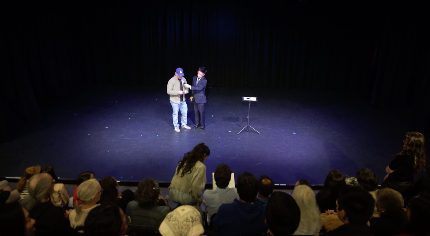 Jacob Martinez on a theater stage with a volunteer in front of a full audience