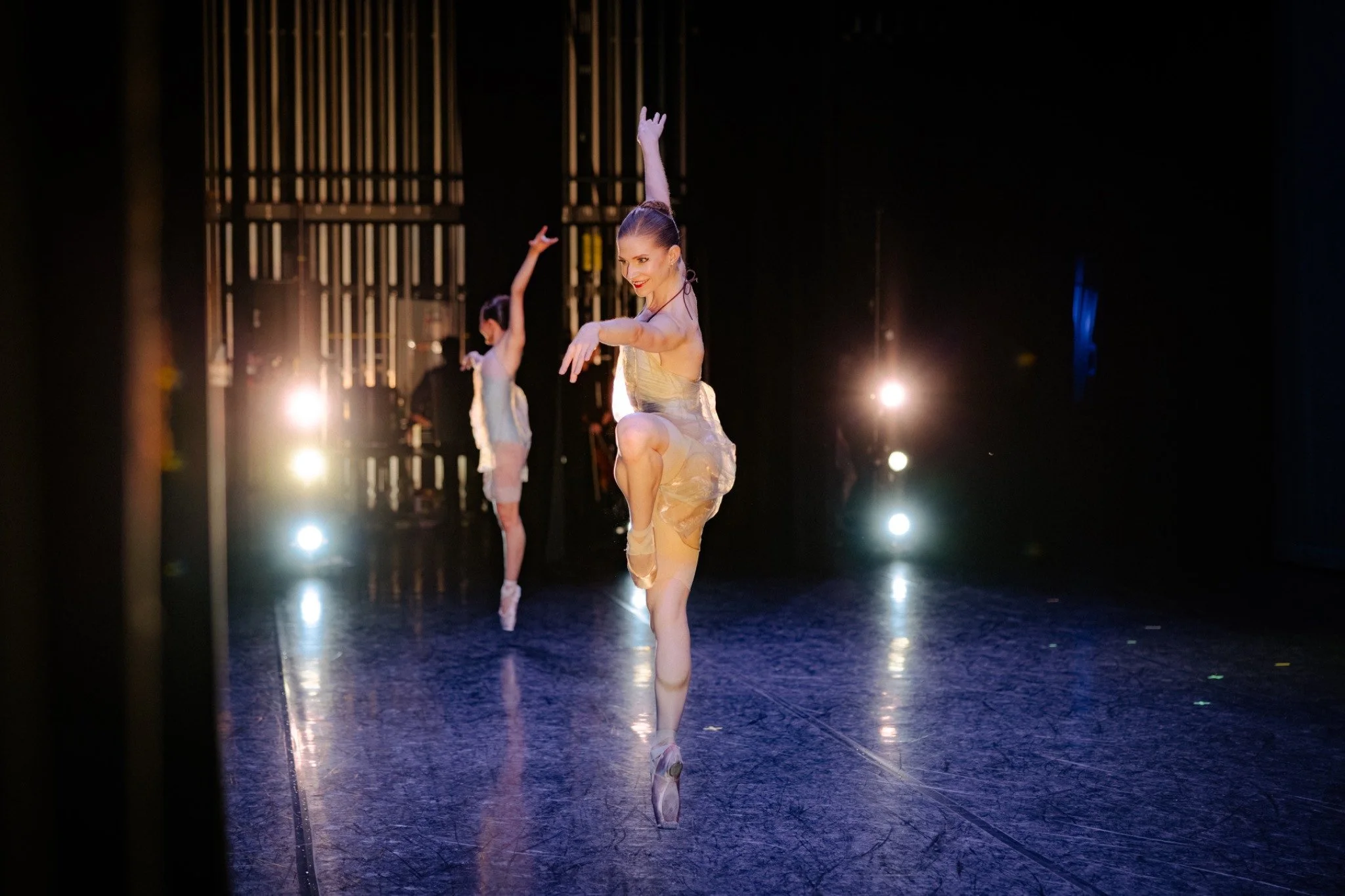 Dancers in pale costumes perform onstage amid warm and cool stage lights.