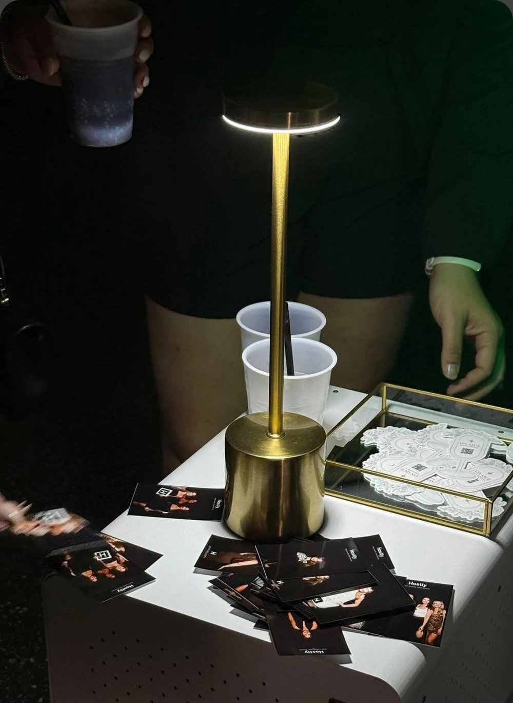 Branded prints and a tray of photo keychains beside a gold lamp at an On Que print station