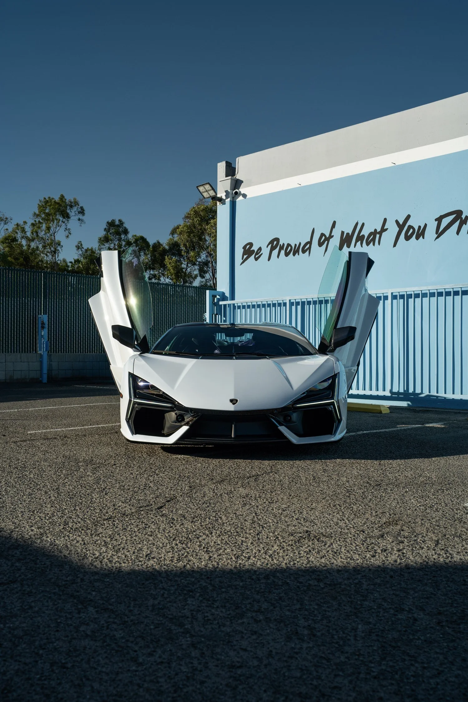 Front view of the white Revuelto with both scissor doors raised outside the studio.
